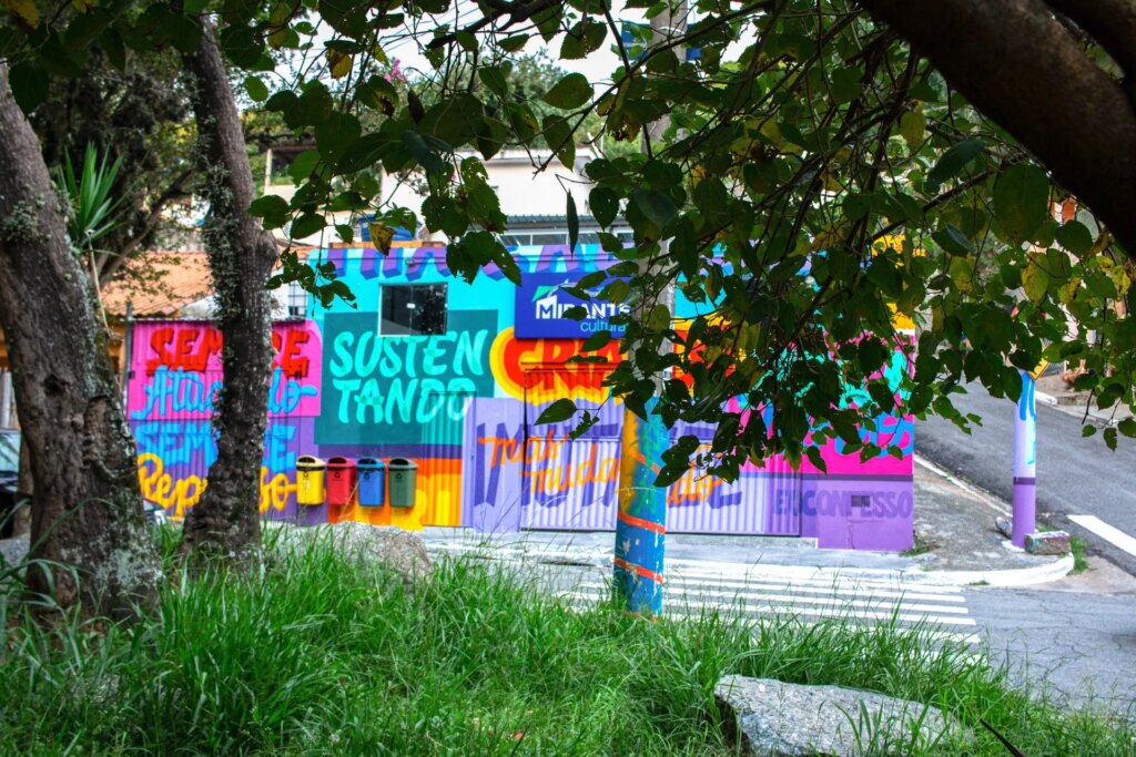 Fachada do Mirante Cultural coberta por grafite colorido, vista entre as árvores da rua na Vila Mirante